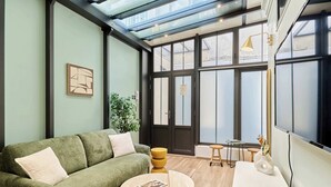 A modern living room with a green sofa, a round wooden table, and a large window with a view. - Sublime AC Apartment 3 bedrooms Saint Germain (Paris)