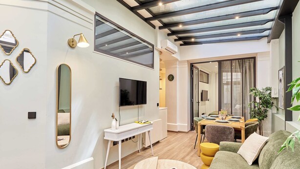 A modern living room with a flat-screen TV, a white console table, a round coffee table, and a green sofa. - Sublime AC Apartment 3 bedrooms Saint Germain (Paris)
