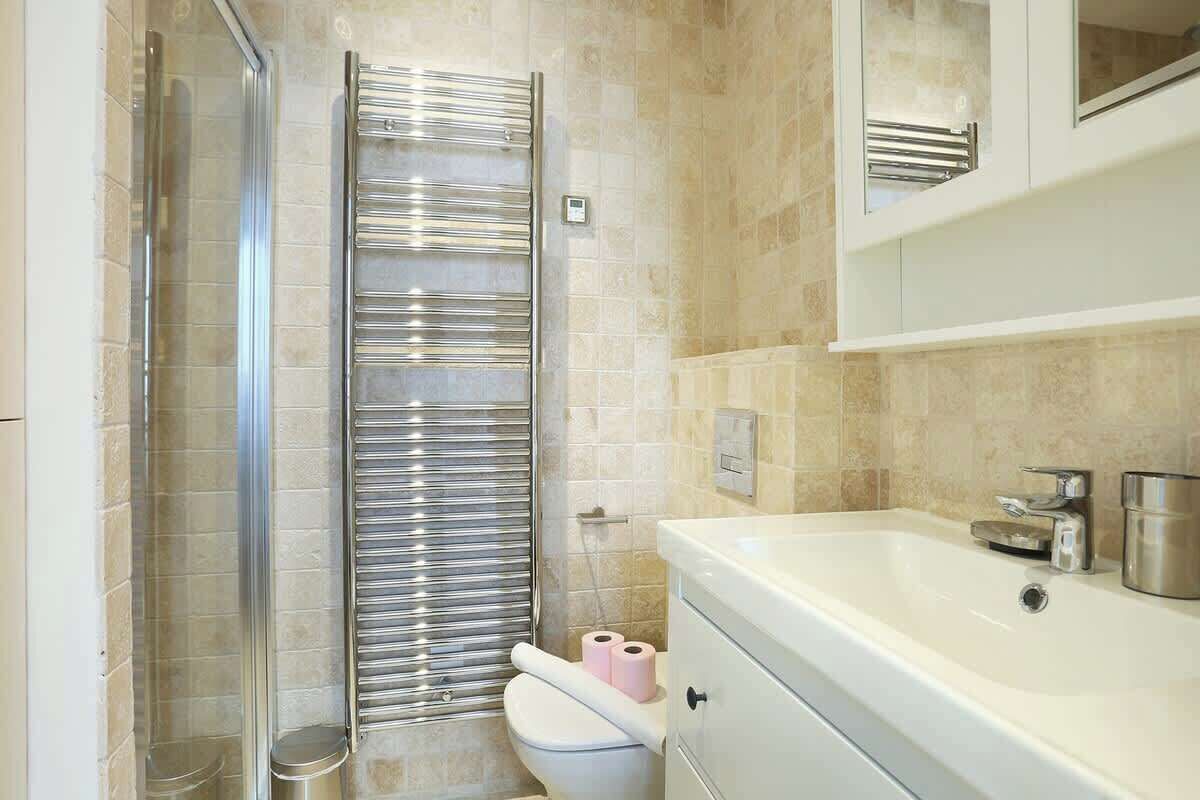 Un baño moderno con cabina de ducha de vidrio, un lavabo blanco con grifo cromado y un inodoro con toallero.