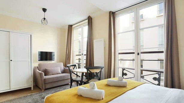 A hotel room with a bed, a sofa, a table, and a TV.