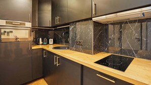 Een moderne keuken met donkere kastjes, een houten aanrechtblad, een inbouwoven, een kookplaat en een marmeren spatwand.