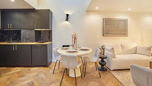 Een moderne keuken met donkere kastjes en een marmeren aanrecht, een eethoek met een ronde tafel en stoelen, en een zithoek met een bank en een abstract kunstwerk aan de muur.