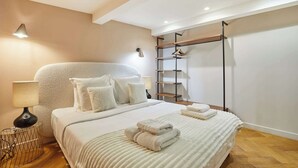 Slaapkamer met een groot bed, een nachtkastje met een lamp, een wandplank en een kledingrek.