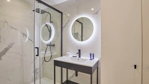 Een moderne badkamer met een douche met glazen wand, een ronde spiegel met ingebouwde verlichting en een wit wastafelmeubel met een zwart aanrechtblad.