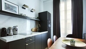 A modern kitchen with dark cabinets, a white countertop, and a dining area with a wooden table and chairs.