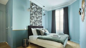 A bedroom with a bed, a wall with a floral pattern, a window with curtains, and a light fixture.