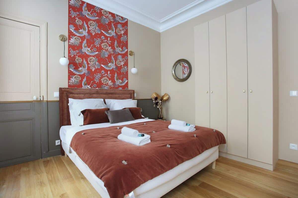 A bedroom with a large bed, a wardrobe, a mirror, and a wall tapestry.