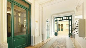 A corridor with green doors, a tiled floor, and a view into another room.