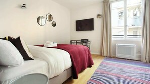 A hotel room with a bed, a flat-screen TV, a small table, and a window with curtains. - Sublime and new Studio Le Marais / Beaubourg (Paris)