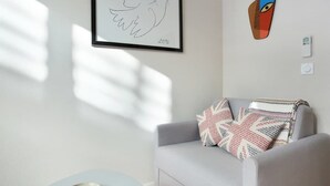 A modern living room with a grey sofa, a framed bird artwork, a geometric wall decoration, and a small table with a decorative item. - Sublime and new Studio Le Marais / Beaubourg (Paris)