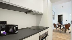 A modern kitchen with white cabinets, a black countertop, and a toaster. There is a dining area with a table and chairs visible in the background. - Elegant Apartment at the Palais Royal Opera (Paris)