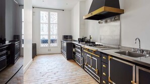 Una cocina moderna con una isla grande, armarios negros, tiradores dorados y una campana extractora de acero inoxidable.