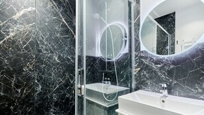 Un baño moderno con ducha envuelta en vidrio, un lavamanos blanco y un salpicadero de mármol.