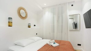 Habitación de hotel con cama, paredes blancas, un espejo y una ventana con cortinas.