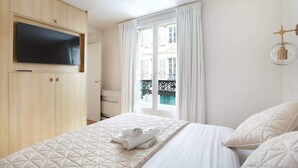 A hotel room with a bed, a TV mounted on a wooden cabinet, a window with curtains, and a balcony view. - Luxurious and new apartment in the center of Paris (Paris)