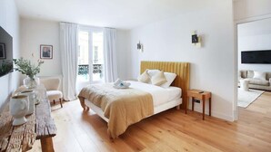 A modern bedroom with a large bed, a wooden nightstand, a small table with a vase, and a view of the outside balcony. - Luxurious and new apartment in the center of Paris (Paris)