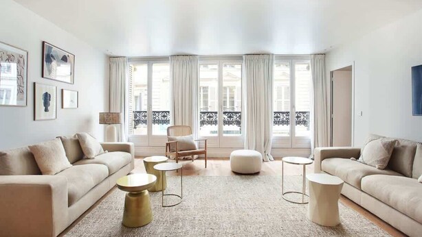 A modern living room with a beige sofa, round coffee tables, and a large window with curtains. - Luxurious and new apartment in the center of Paris (Paris)