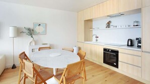 A modern kitchen with wooden cabinets, a round dining table with chairs, and a white countertop. - Luxurious and new apartment in the center of Paris (Paris)