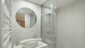 A modern bathroom with a round mirror, a white sink, and a glass shower enclosure.