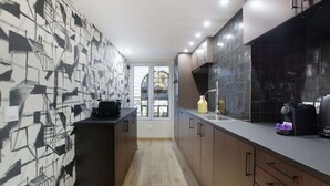 A narrow kitchen with dark cabinets, a black countertop, and a tiled backsplash.