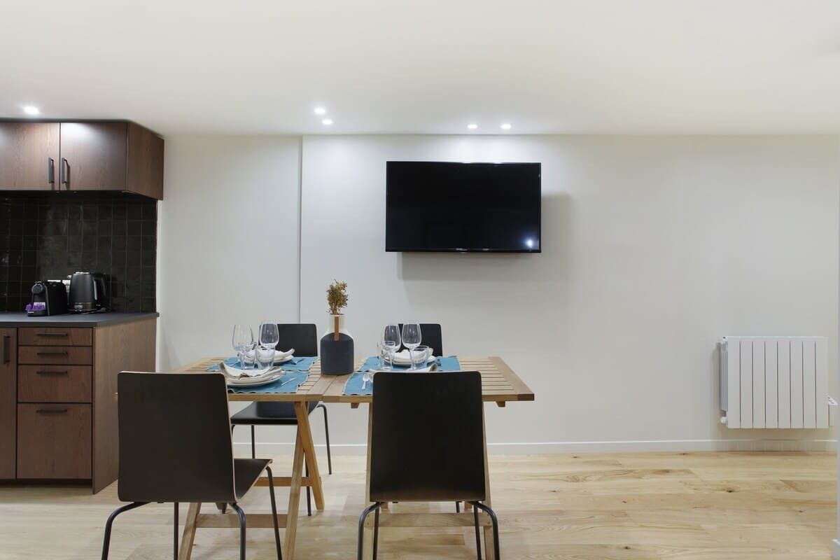 Une cuisine moderne équipée d’un téléviseur à écran plat, de meubles en bois et d’un coin repas avec une table dressée pour quatre personnes.