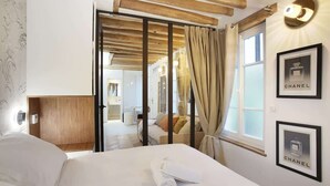 Habitación de hotel con cama, cabecera de madera, ventana con cortinas y cuadros en la pared.