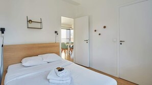 A hotel room with a neatly made bed, a bedside table, a wall-mounted shelf with a plant, and a door with a handle. - Apartment Boulogne facing the "Passage" (Boulogne-Billancourt)