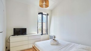 Ein Schlafzimmer mit einem Bett, einem Fernseher auf einer weißen Kommode, einem Fenster mit Aussicht und einer Holzzellentrale.