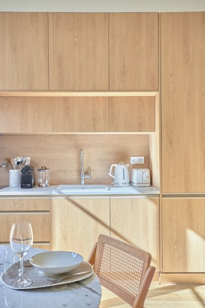 Una cocina moderna con armarios de madera, una encimera blanca y una zona de comedor con una mesa lista para dos.