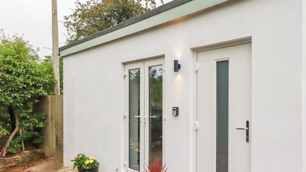 Un bâtiment blanc doté de deux portes vitrées et d’un petit jardin agrémenté de plantes en pot.