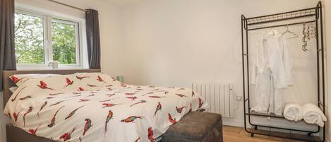 A bedroom with a bed, a window, a radiator, and a clothing rack.