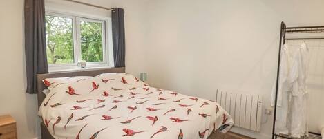 A bedroom with a bed, a window with curtains, a radiator, and a clothing rack.