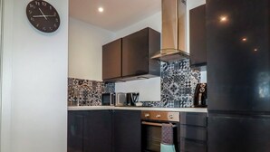 Une cuisine moderne avec des meubles de couleur sombre, un four à micro-ondes, une machine à café et une horloge murale.