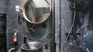 A modern bathroom with a round mirror, a black sink, and a handheld showerhead. - Modern Suite  Center of Paris Montmartre (Paris)