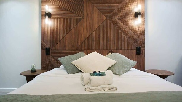 A neatly made bed with pillows and a rolled towel, a wooden geometric wall panel, and two bedside tables with lamps. - Modern Suite  Center of Paris Montmartre (Paris)