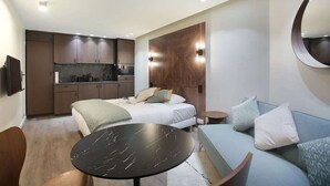 A compact hotel room with a kitchenette, a bed with pillows, a round table, and a sofa. - Modern Suite  Center of Paris Montmartre (Paris)