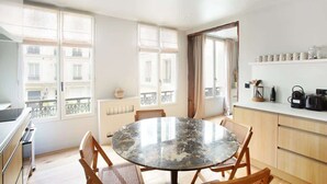 A modern kitchen with a round marble table, wooden chairs, and a built-in oven. - Sublime Apartment AC Paris  Center (Paris)