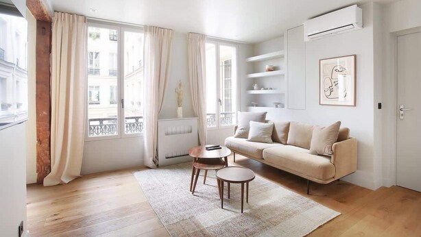A modern living room with a beige sofa, a small round coffee table, and a large window with curtains. - Sublime Apartment AC Paris  Center (Paris)