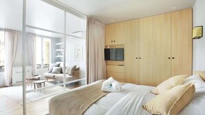 A modern hotel room with a large bed, a sliding glass door leading to a balcony, and a wooden wardrobe. - Sublime Apartment AC Paris  Center (Paris)
