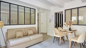 A modern living room with a beige sofa, a dining table with four chairs, and large windows. - Cosy & new apartment Le Marais/Place des Vosges (Paris)