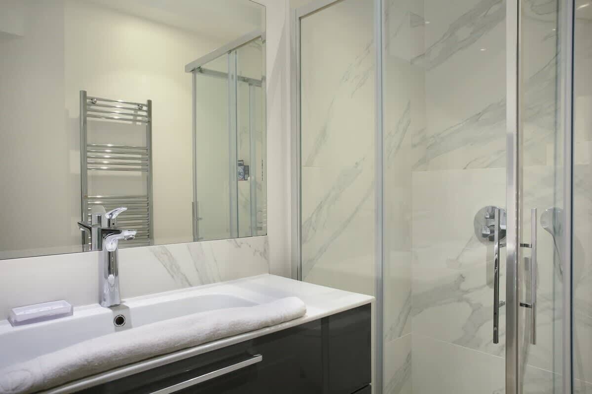 A modern bathroom with a marble sink, a glass shower enclosure, and a large mirror.