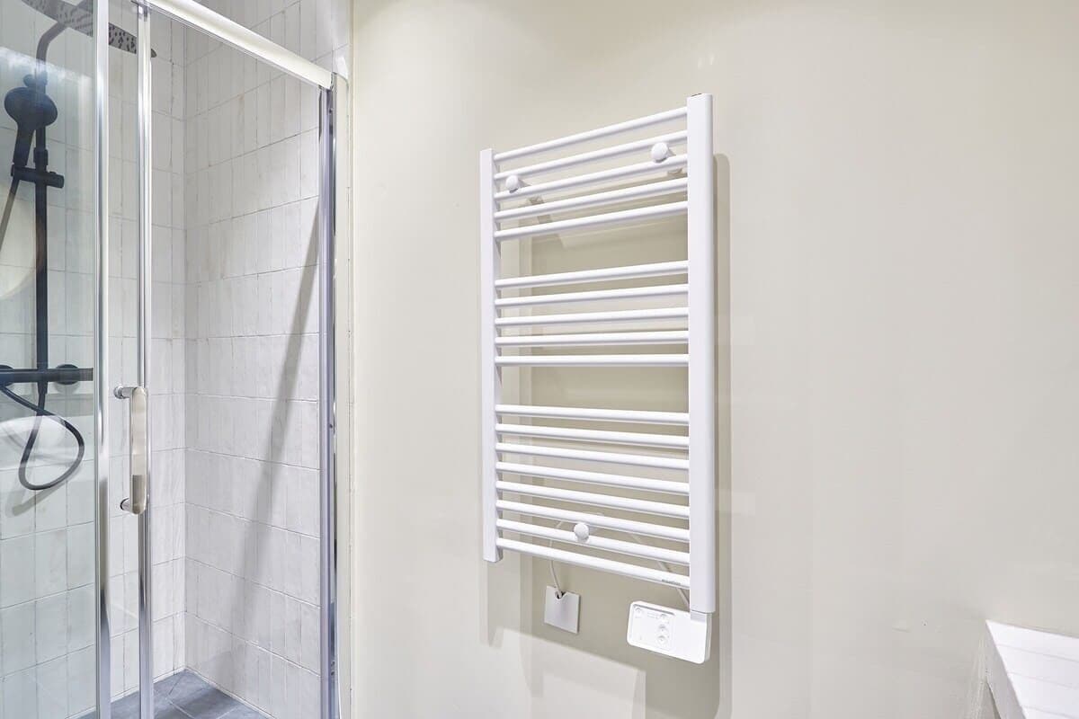 Une salle de bain avec une douche à parois de verre, un porte-serviettes blanc et une prise électrique murale.