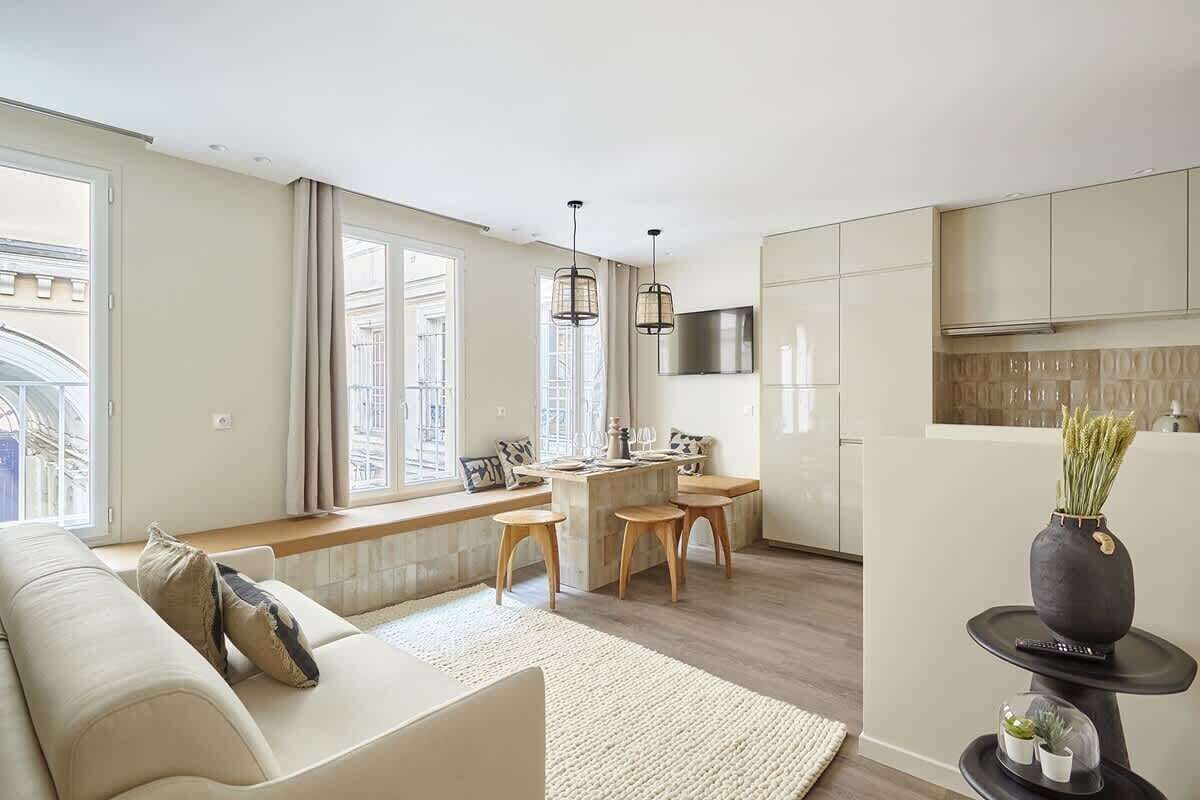 Un salon moderne avec un canapé, un coin repas comprenant une table et des chaises, et une cuisine équipée de meubles et d’un téléviseur.