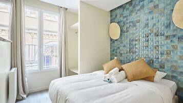 Une chambre d’hôtel avec un grand lit, une fenêtre avec des rideaux, un mur orné d’une mosaïque et un luminaire rond.
