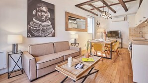 A modern living room with a sofa, a coffee table, and a dining area with chairs and a table. There is a kitchen area with a stove and cabinets. - Charming apartment Center of Paris with terrace (Paris)
