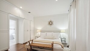 Une chambre avec un lit en bois, du linge de lit blanc, une décoration murale en forme de soleil et une armoire blanche.
