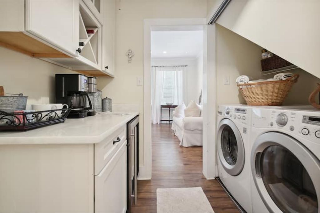 A compact kitchen with a coffee maker, a washing machine, and a dining area in the background.