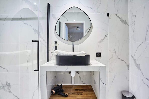 A bathroom with a white marble sink, a round mirror, and a wooden floor.