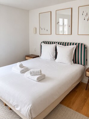 A neatly made bed with white linens and pillows, a striped headboard, and a pair of towels on the bed. - Sublim apartement Saint Germain des Prés (Paris)