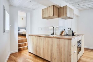 A modern kitchen with wooden cabinets, a central island, and a built-in oven. - Sublim apartement Saint Germain des Prés (Paris)